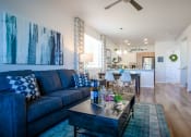 Thumbnail 19 of 32 - a living room with a blue couch and a coffee table in front of a kitchen with a