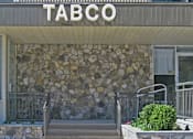 Thumbnail 1 of 9 - The front of a building with a stone wall and a sign that says "TABCO 305".