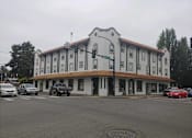Thumbnail 1 of 9 - a white building with a brown roof and cars parked in front of it