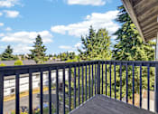 Thumbnail 21 of 42 - A balcony with a metal railing overlooks a parking lot and trees.