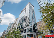 Thumbnail 1 of 26 - A tall building with many windows stands in front of other buildings.