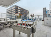 Thumbnail 19 of 26 - A foosball table is on a rooftop patio with chairs around it.