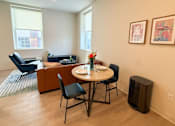 Thumbnail 3 of 20 - A living room with a brown couch, a blue chair, a small table with chairs, and two framed pictures on the wall.at The Jones Tower at the Collective, Pittsburgh, PA 15203
