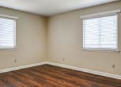 Thumbnail 7 of 25 - A room with wooden floors and two windows with blinds.