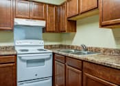 Thumbnail 13 of 25 - A white stove and sink in a kitchen with brown cabinets.