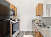 Thumbnail 30 of 54 - A kitchen with a black refrigerator and microwave, wooden cabinets, and a sink.