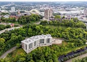 Thumbnail 57 of 64 - A large white building is surrounded by trees in the foreground of a cityscape.