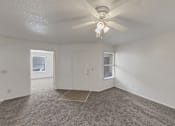 Thumbnail 6 of 27 - A room with a ceiling fan and carpeted floor.