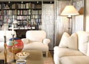 Thumbnail 8 of 25 - A living room with a white couch, a coffee table, and a bookshelf filled with books.