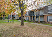 Thumbnail 20 of 33 - A tree with orange leaves stands in front of a brick building with a balcony at A62 Apartments, Indianapolis, IN
