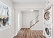 Thumbnail 8 of 32 - A white washing machine is in a laundry room with a staircase.