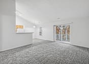 Thumbnail 16 of 54 - A large, empty room with a carpeted floor and a window showing a view of trees outside.