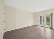 Thumbnail 35 of 54 - A room with a wooden floor and a sliding glass door leading to a green outdoor area.