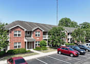 Thumbnail 17 of 21 - A red car is parked in a parking lot in front of a brick building.