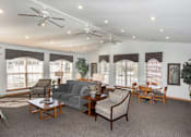 Thumbnail 9 of 21 - A living room with a grey couch, wooden chairs, and a ceiling fan.