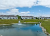 Thumbnail 25 of 40 - A fountain in the middle of a pond in front of a row of houses.