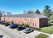 Thumbnail 17 of 17 - A parking lot with cars in front of a brick building.
