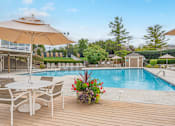 Thumbnail 22 of 46 - A poolside table with chairs and an umbrella overlooking a pool.