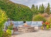 Thumbnail 30 of 46 - A backyard with a stone fire pit and a blue couch.