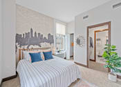 Thumbnail 10 of 49 - A bedroom with a bed, a plant, and a city skyline mural on the wall at Sky Central Apartments, Cincinnati