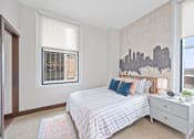 Thumbnail 11 of 49 - A bedroom with a bed, nightstand, and a city skyline mural on the wall at Sky Central Apartments, Cincinnati, OH, 45202