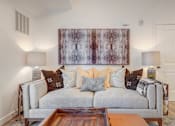 Thumbnail 6 of 38 - A living room with a grey couch and a large abstract painting on the wall.