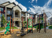 Thumbnail 37 of 38 - A playground with a green slide and a play structure in front of apartment buildings.