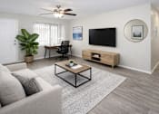Thumbnail 4 of 28 - A living room with a grey couch, a black chair, a wooden coffee table, a flat screen TV, and a wooden cabinet.