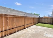 Thumbnail 16 of 18 - A backyard with a wooden fence and a concrete ground.
