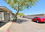 Thumbnail 3 of 18 - A red car is parked on the right side of a street with apartment buildings on the left.