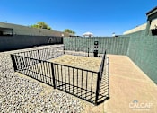 Thumbnail 9 of 18 - A black metal fence encloses a gravel area in a sunny outdoor setting.