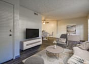 Thumbnail 2 of 13 - A living room with a television, grey chairs, and a white sofa.