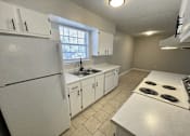 Thumbnail 19 of 27 - A white kitchen with a refrigerator, sink, and stove.