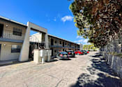 Thumbnail 3 of 27 - A parking lot with cars and a building with a white facade.