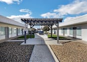 Thumbnail 11 of 17 - A modern building with a gravel pathway leading to a covered walkway.