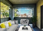 Thumbnail 8 of 20 - A living room with a grey couch, a white coffee table, and a large window with a view of trees.