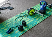 Thumbnail 8 of 18 - A green mat with a kettlebell, dumbbells, and resistance bands on it.