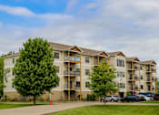 Thumbnail 12 of 18 - A large apartment building with a parking lot in front.