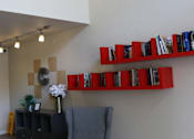 Thumbnail 7 of 18 - A living room with a grey couch and a red shelf with books.