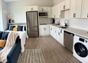Thumbnail 18 of 35 - a living room with a couch and a kitchen with a sink and refrigerator