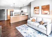 Thumbnail 6 of 35 - A modern living room with a white couch and a kitchen area in the background.