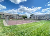 Thumbnail 11 of 35 - The tennis court at Olde English Village, surrounded by well-kept grounds and nearby apartment buildings.