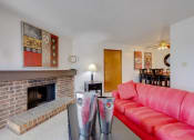 Thumbnail 27 of 35 - Living room in the one-bedroom model unit at Olde English Village, featuring a stone-brick fireplace and cozy seating.