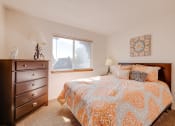 Thumbnail 19 of 35 - Bedroom in the two-bedroom model unit at Olde English Village, featuring a comfortable bed and soft lighting.