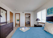 Thumbnail 21 of 35 - Bright bedroom in the two-bedroom model unit at Olde English Village, showcasing a large window and well-appointed furnishings.