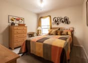 Thumbnail 13 of 16 - Cozy bedroom with a natural wood bed and dresser, beige walls, quilted bedding, a window bringing in natural light, and carpeted floors.