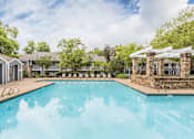 Thumbnail 7 of 25 - A large swimming pool surrounded by trees and a stone building.