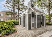 Thumbnail 14 of 25 - A small grey building with a clock tower sits in the middle of a brick walkway.