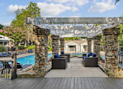 Thumbnail 5 of 20 - A wooden deck with a stone archway leading to a patio area with a pool.