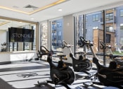 Thumbnail 45 of 65 - a gym with several exercise bikes in front of a window at Stonehill at West Orange, West Orange, NJ, 07052